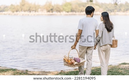 Asian couple walking in garden with picnic basket. in love couple is enjoying picnic time in park outdoor Royalty-Free Stock Photo #2281194095