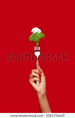 Food pop art photography. Female hand holding broccoli on fork against red studio background. Healthy eating. Concept of art and creativity. Complementary colors. Copy space for ad, text