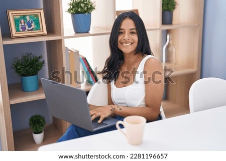 Young hispanic woman using laptop sitting on table at home