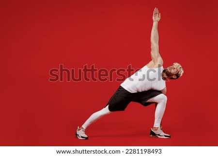 Full body young strong sporty toned sportsman man wear white clothes spend time in home gym training doing side plank exercise pilates isolated on plain red background. Workout sport fit body concept