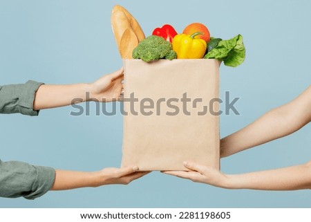 Close up cropped female hold in hand brown paper bag with food products isolated on blue color wall background studio. Delivery service from shop or restaurant concept. Copy space advertising mock up Royalty-Free Stock Photo #2281198605