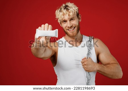 Young happy confident strong sporty toned sportsman man wear white clothes spend time in home gym hold metal chain protein energy bar isolated on plain red background. Workout sport fit body concept