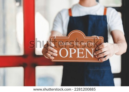 The store owner holds a sign in front of the store ready to serve.