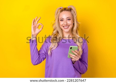Photo portrait of lovely young lady show okey symbol fingers hold gadget wear trendy purple clothes isolated on yellow color background