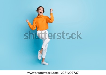 Full body photo of attractive young woman raise fists celebrate win lottery dressed stylish orange look isolated on blue color background