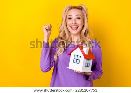 Photo of pretty lucky lady dressed purple shirt rising little house rising fist isolated yellow color background