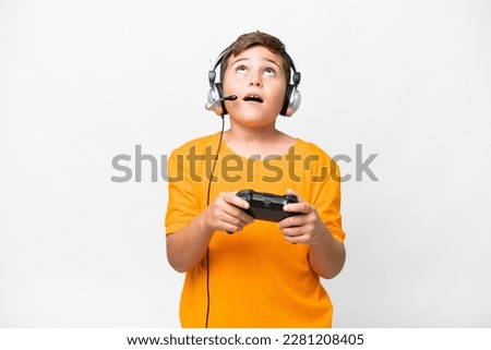 Little caucasian kid playing with a video game controller over isolated white background looking up and with surprised expression