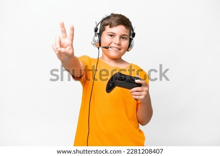 Little caucasian kid playing with a video game controller over isolated white background smiling and showing victory sign