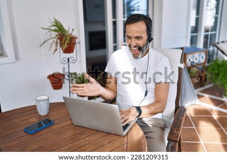 Middle age man wearing call center agent headset working from home celebrating achievement with happy smile and winner expression with raised hand 