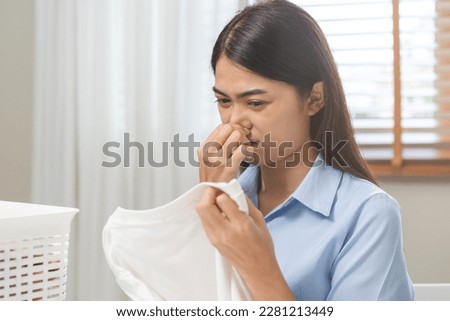 Asian young housewife woman having bad smelling clothes holding breath nose with fingers, sniff smelly dirty stinky musty, look disgusting from clothes after washed clothes, laundry out of machine. Royalty-Free Stock Photo #2281213449