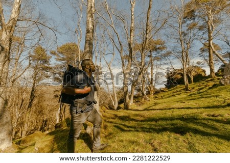 Horizontal photo of black man hiking intently up the rocks of green lush mountainside on bright sunny morning
