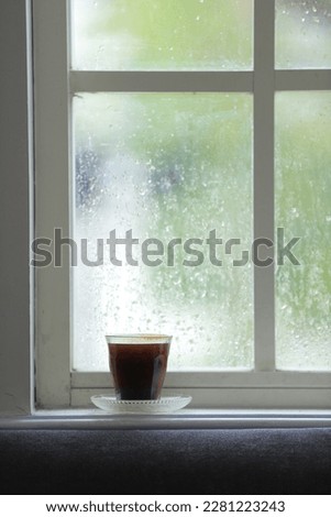 A glass of black coffee on the Window Sill, with against the warm light from the sunny day outside. Royalty-Free Stock Photo #2281223243