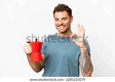Brazilian man holding coffee pot over isolated white background showing ok sign with fingers