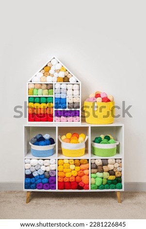 Shelving with storage baskets and colored balls of yarn for knitting. Bright yarn balls lined up on the shelves. Organizing and storage in craft room. Handmade, needle craft, creativity and  hobby.  Royalty-Free Stock Photo #2281226845