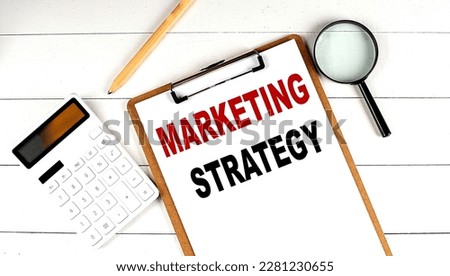 MARKETING STARATEGY words on clipboard, with calculator, magnifier and pencil on white wooden background