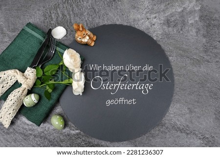 Easter decorations with flowers, Easter eggs, cutlery, and an inscribed slate plate. German inscription means we are open over the Easter holidays. Royalty-Free Stock Photo #2281236307