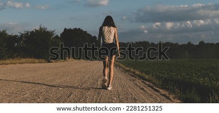 A young girl walks along a country road during sunset