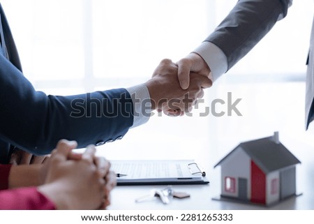 Real estate agent shaking hands with a client to sign a home purchase contract and congratulate the client.
