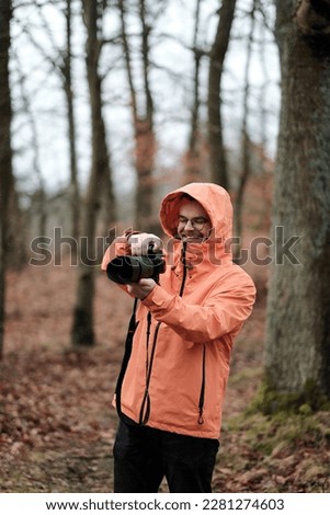 A young and smiling male while taking photos of the forest around him. Progressive photographer with a modern and expensive mirrorless camera. A man holding a camera with a telezoom lens in his hands.