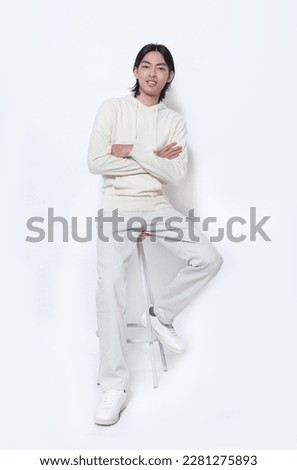 Full body portrait of young man wearing white hoodie with khaki pants sitting chair on white background