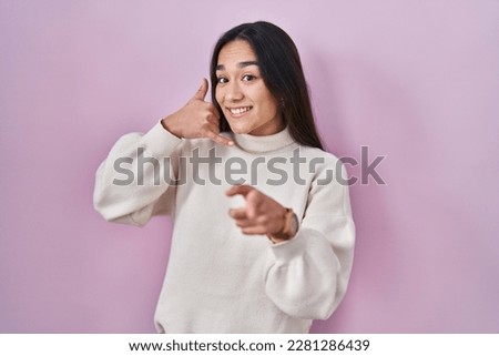 Young south asian woman standing over pink background smiling doing talking on the telephone gesture and pointing to you. call me. 