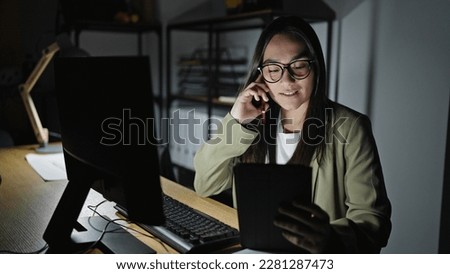Young beautiful hispanic woman business worker using tablet talking on smartphone at office