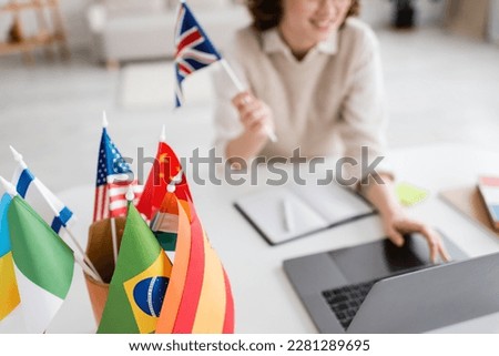 selective focus of international flags near teacher of foreign languages using laptop on blurred background
