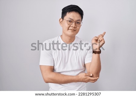 Young asian man standing over white background with a big smile on face, pointing with hand finger to the side looking at the camera. 