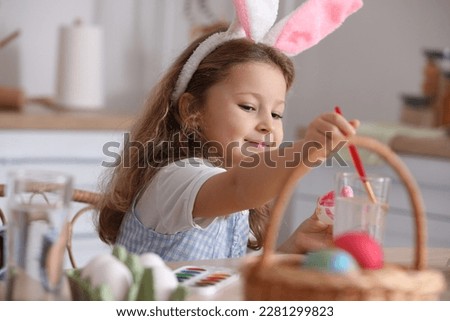 Little girl painting Easter egg at table in kitchen, closeup
