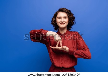 brunette woman smiling and showing gesture meaning stand on sign language isolated on blue