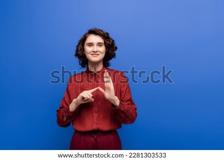 happy young teacher showing alphabet on sign language and looking at camera isolated on blue