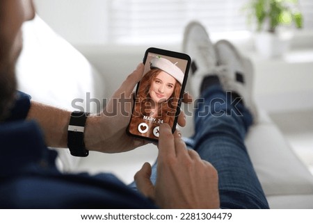 Man viewing female profile on dating site via mobile phone at home, closeup