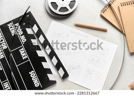 Movie clapper with storyboard, notebooks and film reel on light background Royalty-Free Stock Photo #2281312667