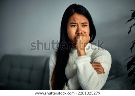 A sensitive adult Asian woman sitting alone on a couch at home, with a hand over her mouth and watching a drama movie. Royalty-Free Stock Photo #2281323279