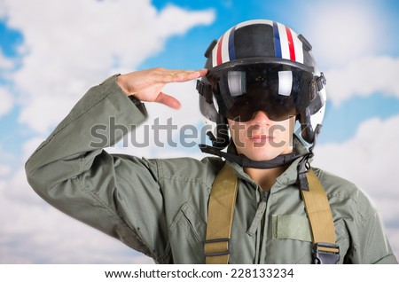 closeup portrait of young pilot wearing helmet saluting with a sky background
