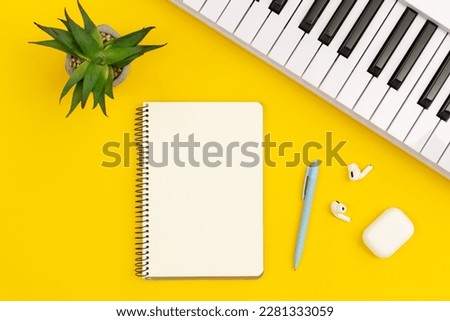 Piano and notebook on yellow background, flat lay, musical creativity concept, copy space.