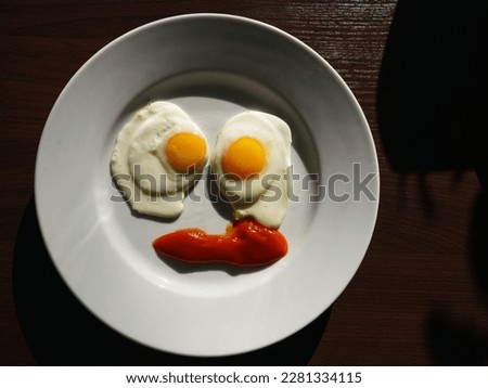 Photography of two fried eggs on plate. They are like eyes. The mouth is drawn with ketchup. Like sleepy face. Delicious traditional breakfast. Concept of good morning. Close up image. View from above