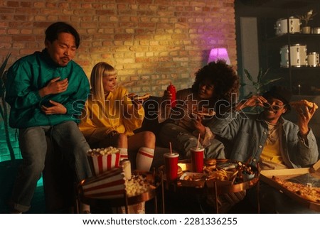 A group of 90s retro styled friends are at home enjoying eating takeout food on a sofa. Royalty-Free Stock Photo #2281336255