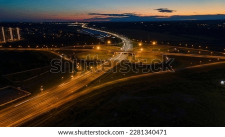 Aerial view of the bigger traffic interchange with many cars next to forest and the historical and at same time modern city of St. Petersburg at light summer night, fog