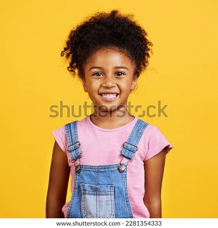 Studio portrait of girl looking standing alone isolated against a yellow background. Cute hispanic child posing inside. Happy and cute kid smiling and looking carefree in casual clothes Royalty-Free Stock Photo #2281354333