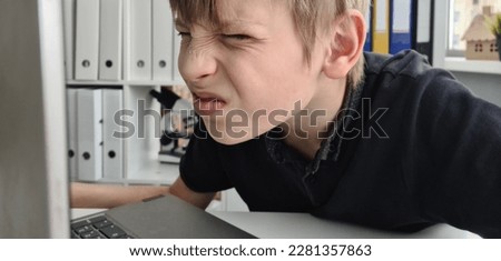 Teenager boy squints using a laptop with poor eyesight sits and looks at computer. Online student at home Royalty-Free Stock Photo #2281357863