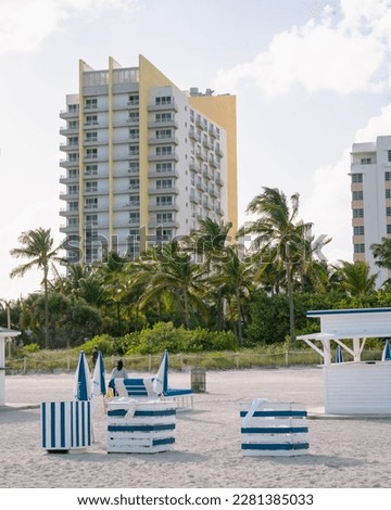Miami Beach and skyscraper. Blue and white stripe chairs, umbrellas, and beach huts. 