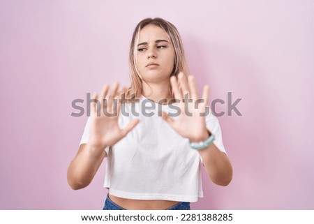 Young blonde woman standing over pink background moving away hands palms showing refusal and denial with afraid and disgusting expression. stop and forbidden. 