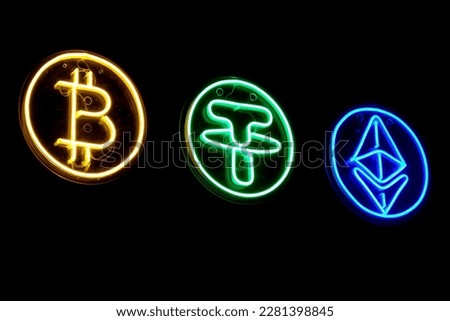 Close-up of neon signs in the form of logos of famous crypto-currencies on a dark background in a night city.