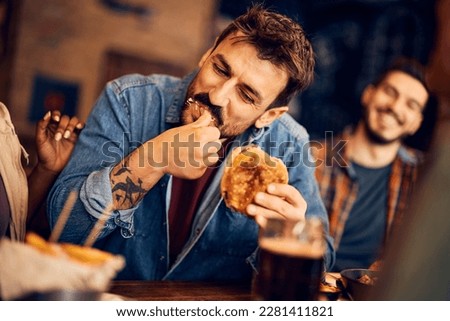 Young happy man eating burger and having fun with friends in a bar.