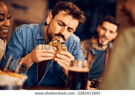Hungry man eating burger while gathering with friends in a pub. Royalty-Free Stock Photo #2281411843