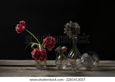 Flowers in small glass bottles on an old wooden table. Still life with tulips and glass vases on a dark background. Dark photo with flowers. High quality horizontal photo with overturned vase
