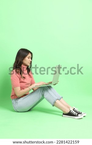 The young adult Asian woman with casual clothes with jeans sitting on the green background.