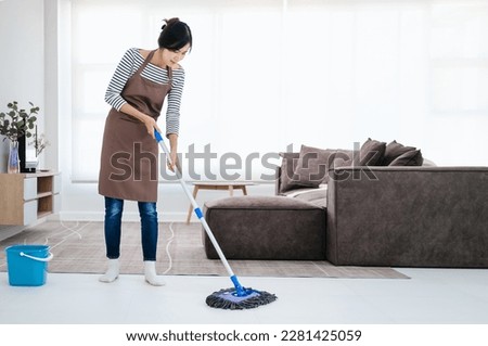 Attractive young Asian woman mopping tile floor at living room while doing cleaning at home during Staying at home using free time about their daily housekeeping routine. Royalty-Free Stock Photo #2281425059