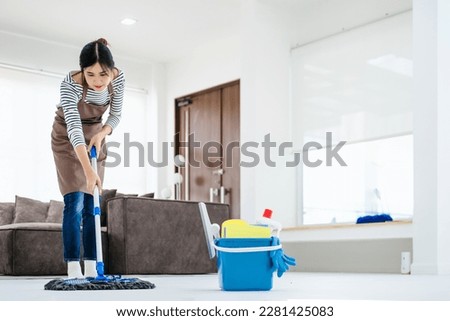 Pretty young lady in apron wiping floor with mop, doing house cleanup living room, free space. Positive housewife tidying her apartment, doing household chores. Professional sanitary service concept.